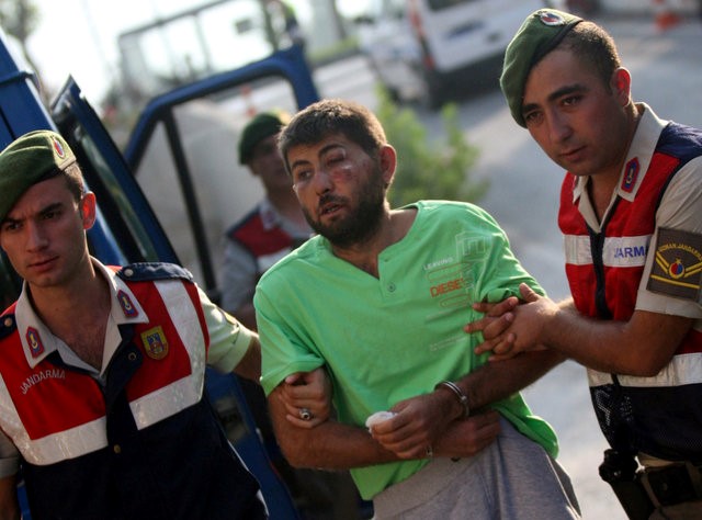 © Reuters. Turkish gendarmeries escort one of the 11 fugitive commandos who were involved in a bid to seize President Tayyip Erdogan during a failed coup attempt last month, as he arrives at the police headquarters in Mugla