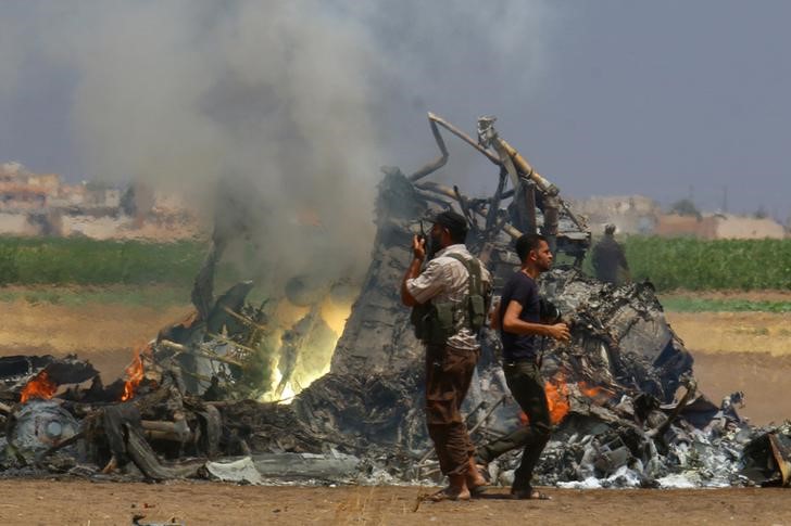 © Reuters. Homens olhando destroços de helicóptero russo derrubado na província síria de Idlib