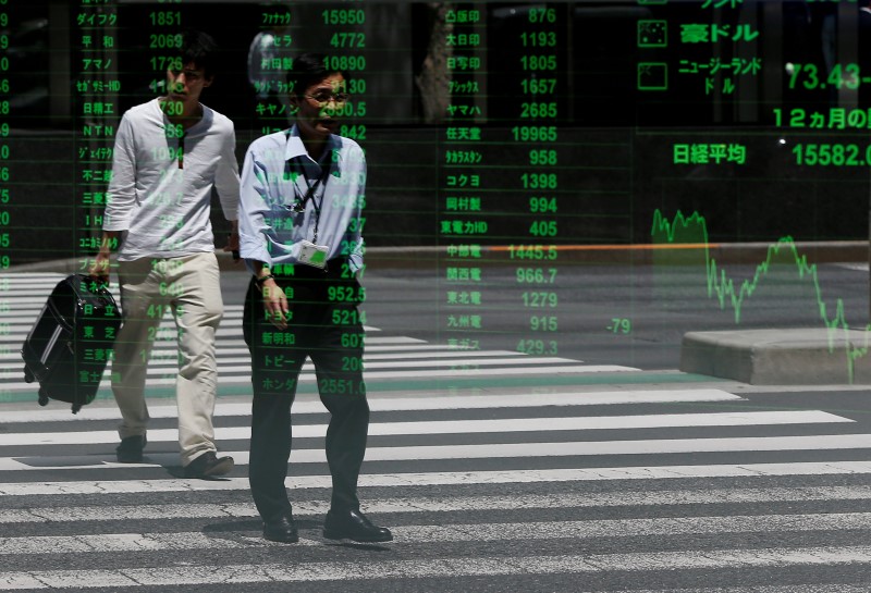 © Reuters. Passersby are reflected on a stock quotation board outside a brokerage in Tokyo, Japan