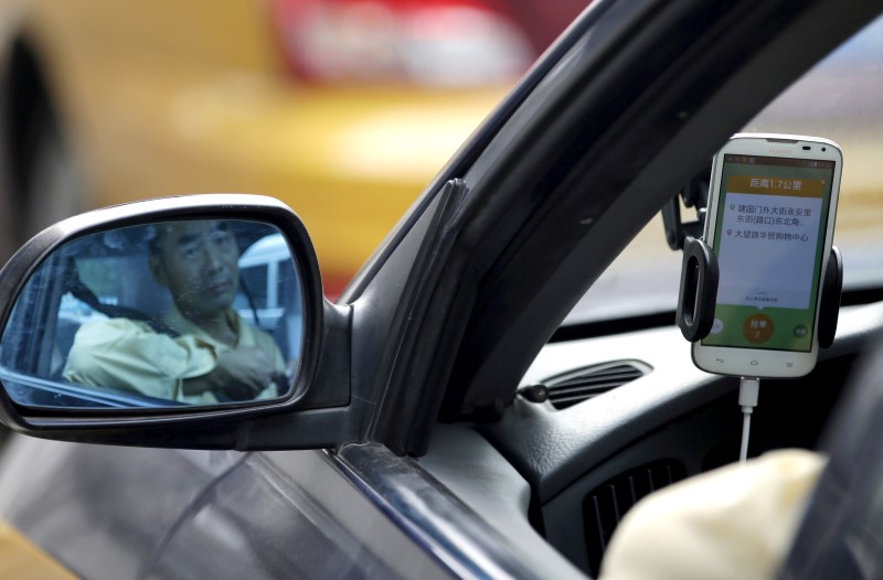 © Reuters. A taxi driver is reflected on a side mirror as he uses Didi Chuxing car-hailing application in Beijing