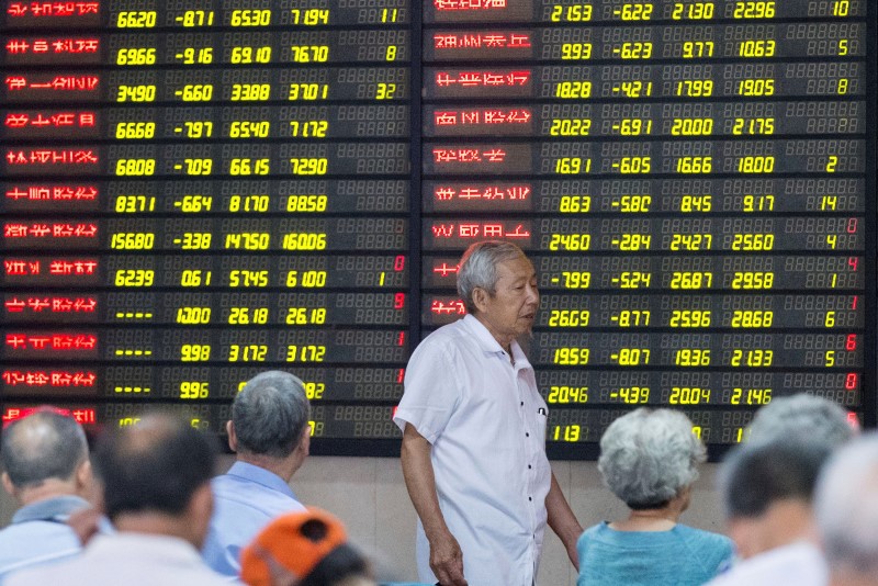 © Reuters. An investor walks past an electronic board showing stock information at a brokerage house in Nanjing