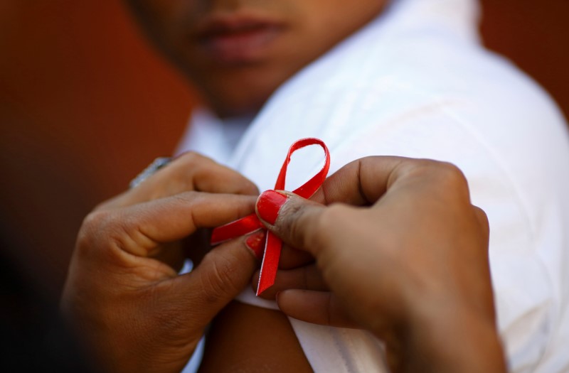© Reuters. A red ribbon is put on the sleeves of a man by his friend to show support for people living with HIV during a program to raise awareness about AIDS on World AIDS Day in Kathmandu