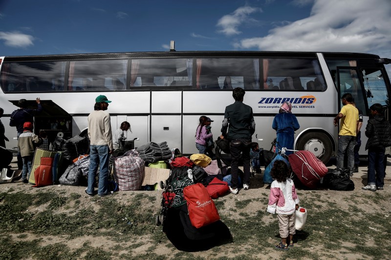 © Reuters. Syrian refugees stand near a bus as they wait to be transferred to a hospitality centre during a police operation at a makeshift camp for refugees and migrants at the border between Greece and Macedonia, near the village of Idomeni