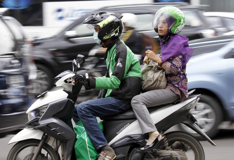 © Reuters. Woman rides on the back of a motorbike, part of the Go-Jek ride-hailing service, on a busy street in central Jakarta