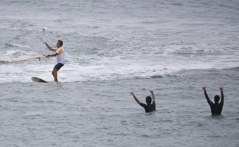 © Reuters. Brazilian surfer Rico de Souza carries the Olympic torch as he surfs at praia da Macumba (Macumba beach) in Rio de Janeiro