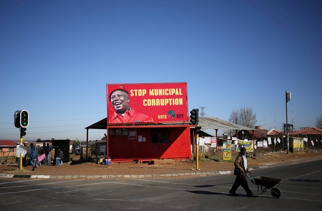 © Reuters. A man pushes a wheelbarrow past a billboard of the Economic Freedom Fighters (EFF), which is led by Julius Malema, Zuma's one-time protege and a former ANC youth leader, in Soweto, South Africa