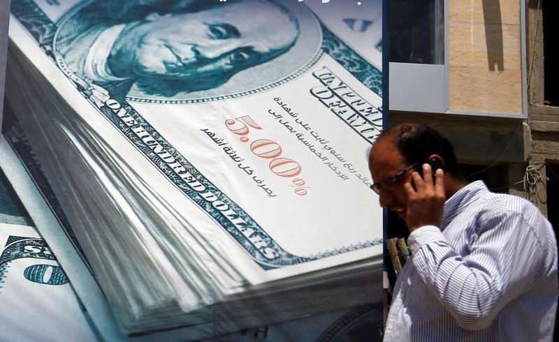 © Reuters. A man talks on his mobile phone as he walks in front of the construction of a new bank building covered with an image of the U.S dollar in Cairo