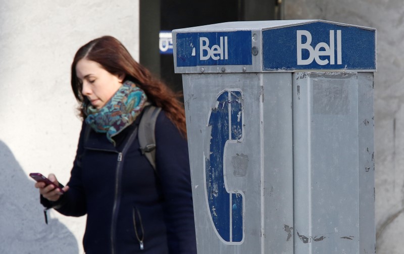 © Reuters. A woman uses a mobile device while walking past a Bell payphone in Ottawa