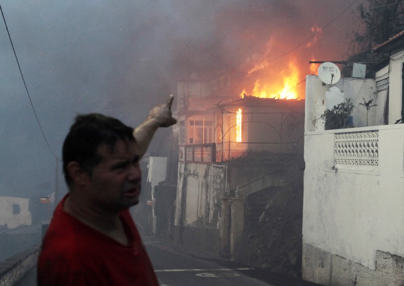 © Reuters. A man gestures as house burns as a wildfire spreads at Bom Sucesso in Funchal, Madeira island,