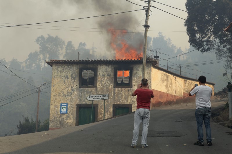 © Reuters. Homens tiram foto de casa em chamas em Funchal, na Ilha da Madeira