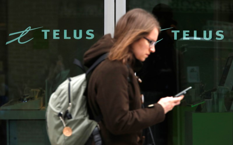 © Reuters. A woman uses a mobile device while walking past a Telus store in Ottawa