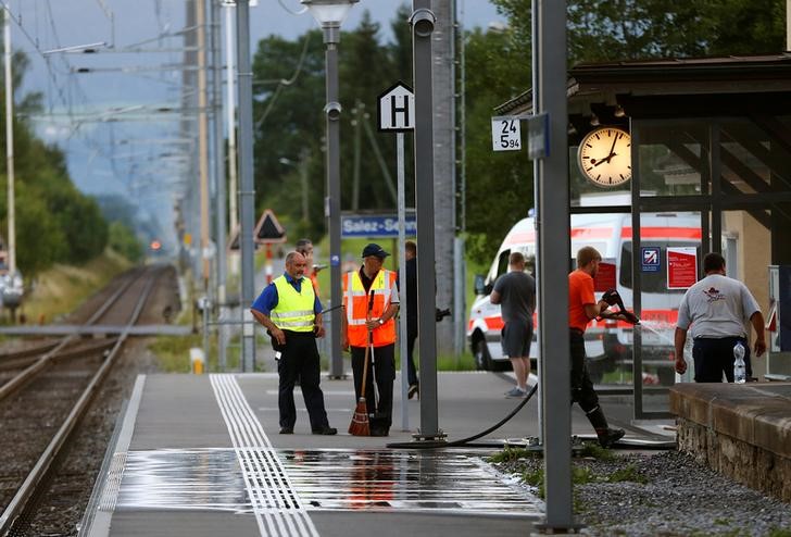 © Reuters. A Swiss police officer stands near workers cleaning a platform after a 27-year-old Swiss man's attack on a Swiss train at the railway station in the town of Salez