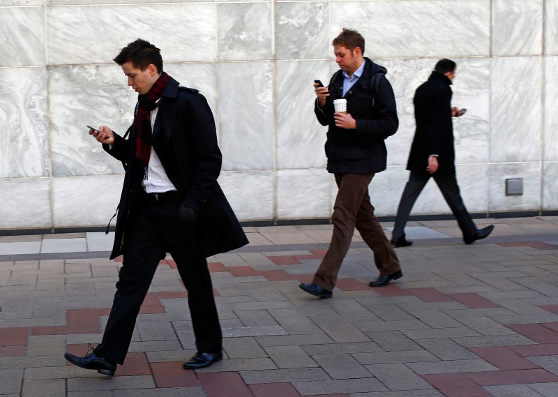 © Reuters. Workers look at their phones while walking at the Canary Wharf business district in London