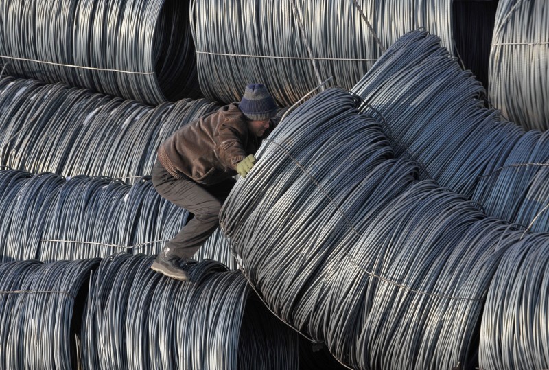 © Reuters. A worker stands on steel wire rod coils at a steel market in Shenyang