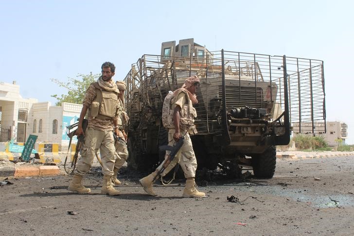 © Reuters. Yemeni army soldiers walk past a damaged armoured personnel carrier in Yemen's southern city of Zinjibar after army forces took it over from militants