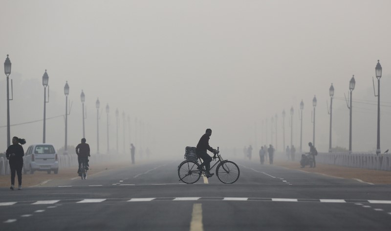 © Reuters. A newspaper vendor rides his bicycle on a smoggy morning in New Delhi