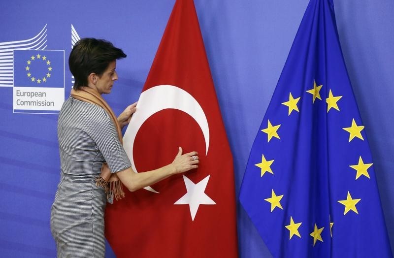 © Reuters. A woman adjusts the Turkish flag next to the EU flag before the arrival of Turkish PM Davutoglu at the EU Commission headquarters in Brussels