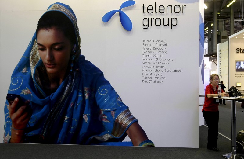 © Reuters. A visitor rests under a Telenor Group sign at the GSMA Mobile World Conference in Barcelona