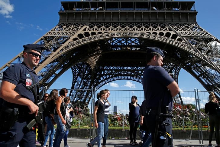 © Reuters. French CRS policemen patrol as tourists walk past in front of the Eiffel Tower in Paris