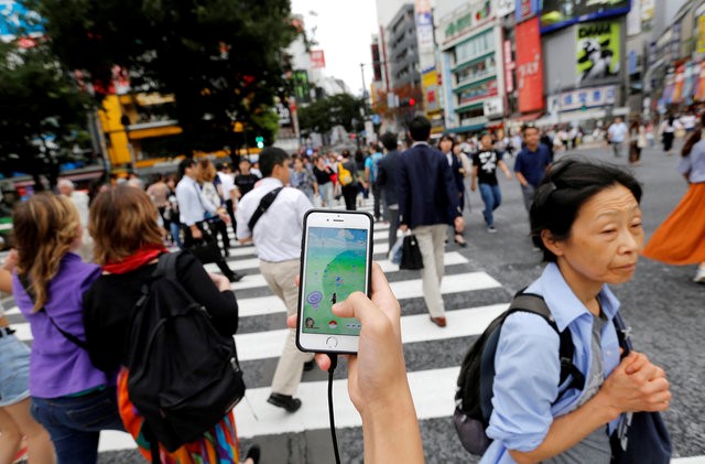 © Reuters. A man plays the augmented reality mobile game "Pokemon Go" by Nintendo on his mobile phone as he walks at a busy crossing in Shibuya district in Tokyo