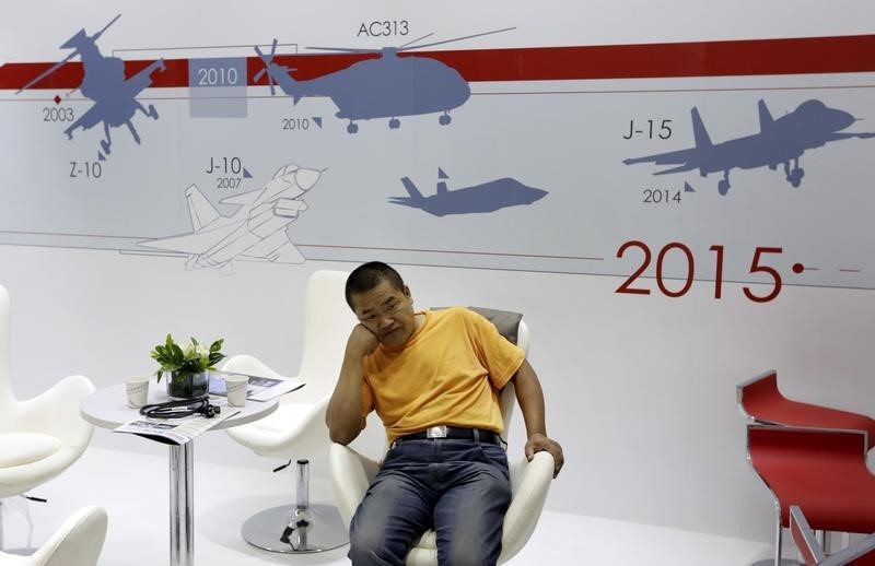 © Reuters. A visitor rests next to a billboard showing the signs of Chinese Air Force's fighters and helicopters at the Aviation Expo China 2015 in Beijing