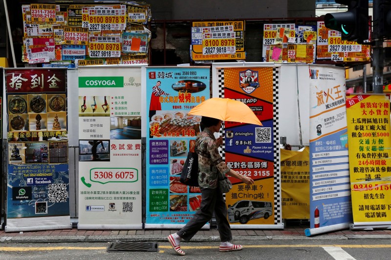 © Reuters. A woman walks past banners promoting retail goods and services displayed in front of closed shops for rent at the shopping Mongkok District in Hong Kong