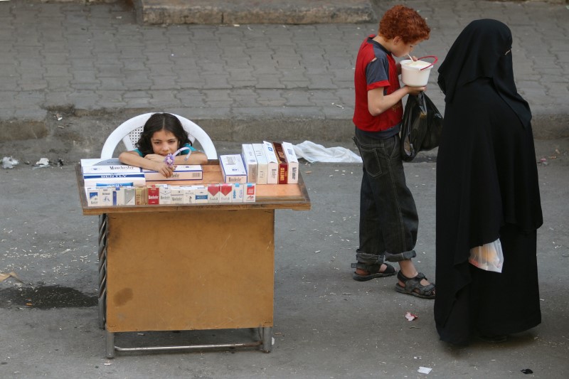 © Reuters. A boy eats yogurt near a girl selling cigarettes in the rebel held al-Shaar neighborhood of Aleppo