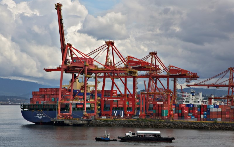 © Reuters. A tugboat pulling a transport truck on a barge crosses the harbour beside the container port in Vancouver