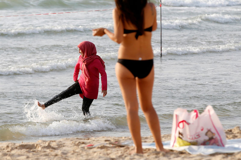 © Reuters. A Muslim woman wearing a Hijab kicks the water in the Mediterranean Sea as a woman wearing a bikini stands nearby at the beach in Tel Aviv, Israel