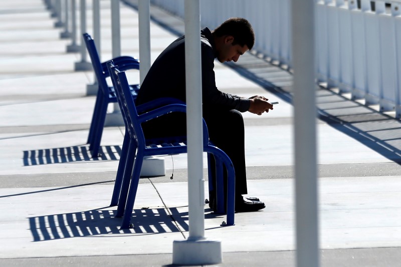 © Reuters. A man types on his mobile phone as he sits along a boardwalk in San Diego