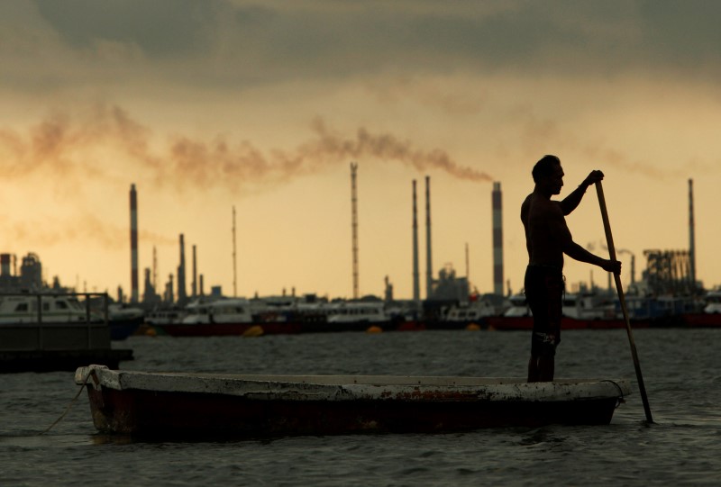 © Reuters. A fisherman rows his dinghy past oil refineries near port terminals in Singapore