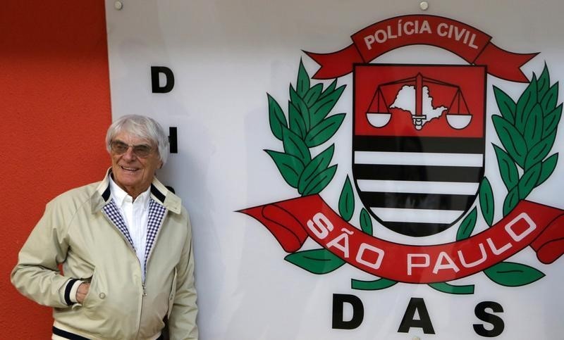 © Reuters. Formula One chief Bernie Ecclestone poses next to a police logo at police central station in Sao Paulo