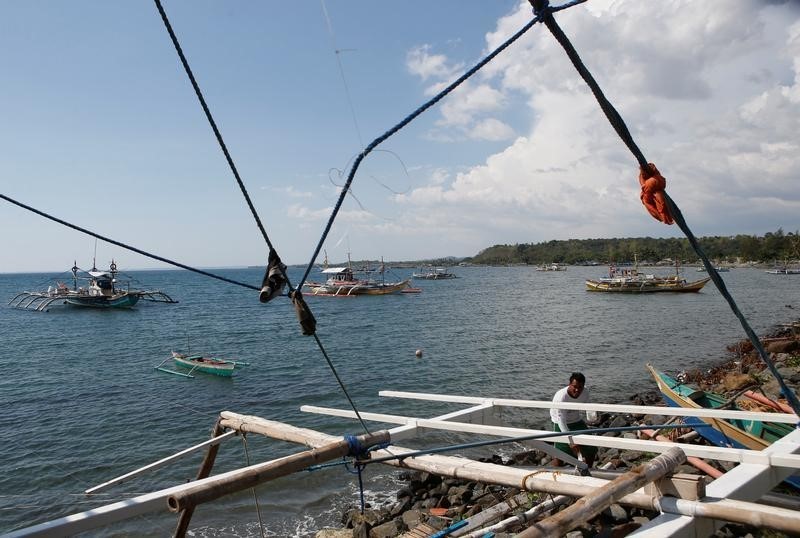 © Reuters. A fisherman repairs his boat overlooking fishing boats that fish in the disputed Scarborough Shoal in the South China Sea, at Masinloc, Zambales, in the Philippines