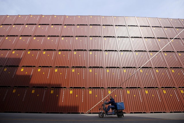 © Reuters. A man rides a vehicle past container boxes at a port in Shanghai