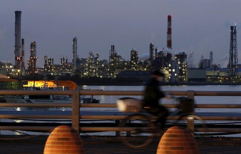 © Reuters. A man rides on a bicycle past chimneys at factories at the Keihin industrial zone in Kawasaki