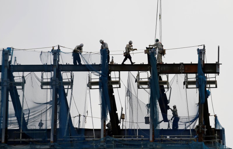 © Reuters. Laborers work under cranes at a construction site for a new commercial building in Tokyo