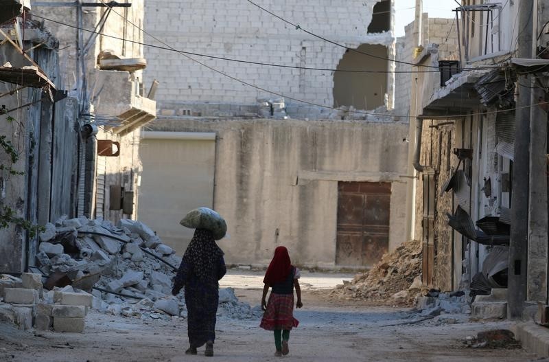 © Reuters. Civilians walk past damaged buildings in the rebel-held al-Sheikh Said neighbourhood of Aleppo