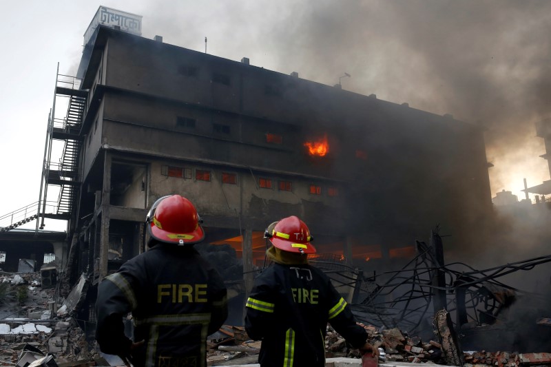 © Reuters. Firefighters stand at the site of a fire at a packaging factory outside Dhaka