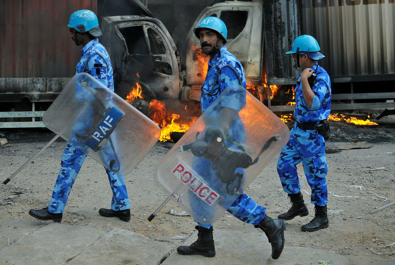 © Reuters. Members of the security forces make their way past burning lorries in Bengaluru