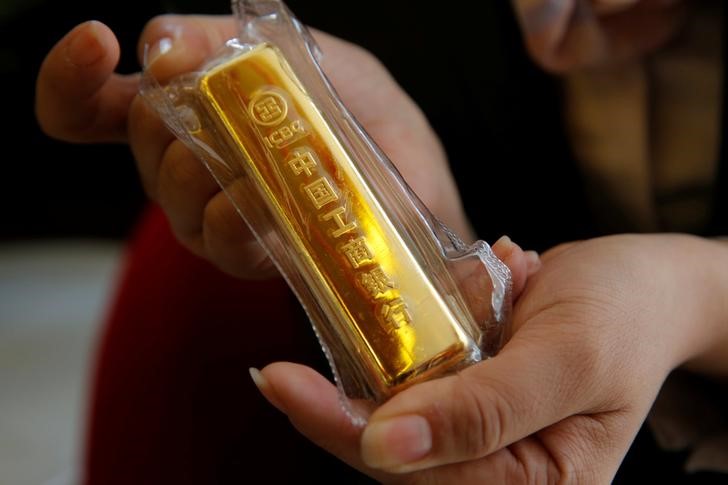 © Reuters. An employee of ICBC bank displays a gold bar as she poses for a photograph during a photo opportunity at its branch in Beijing