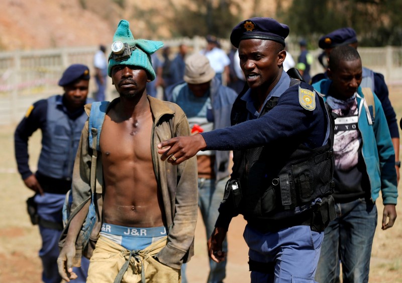 © Reuters. A police officer gestures to a suspected illegal miner after he surfaced from an underground Johannesburg's oldest gold mine in Langlaagte