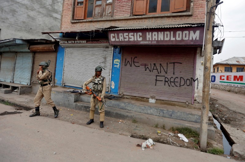 © Reuters. Indian policemen stand guard near a shop with its shutters sprayed with graffiti in Srinigar