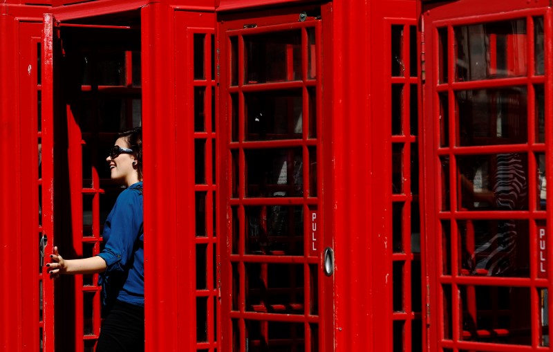 © Reuters. A woman poses in the door of a row  traditional red telephone boxes in central London