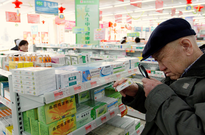 © Reuters. An elderly man uses a magnifiying glass to see the description on a pack of medicine at a pharmacy in Dandong