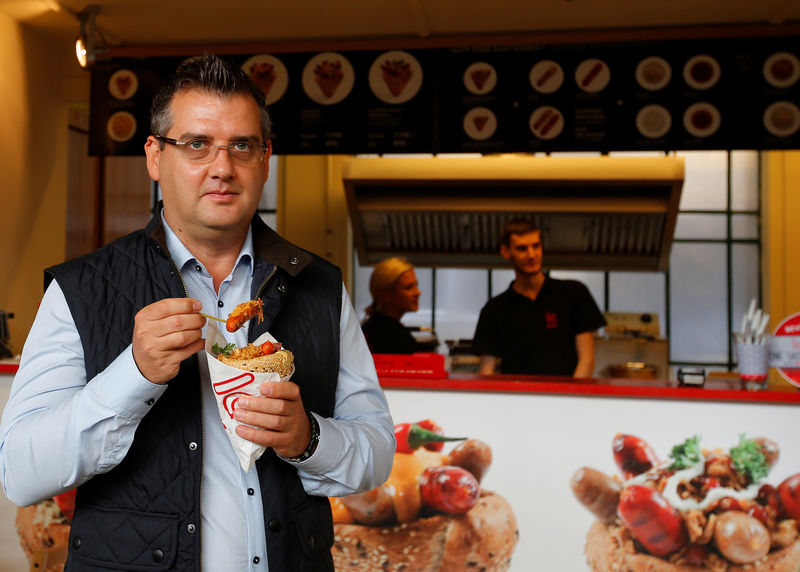 © Reuters. Behovits, owner and managing director of Hungarian firm Kobe Sausages, eats "kolbice", mini sausages and toppings stuffed in a cone-shaped bun, in a market hall in Budapest