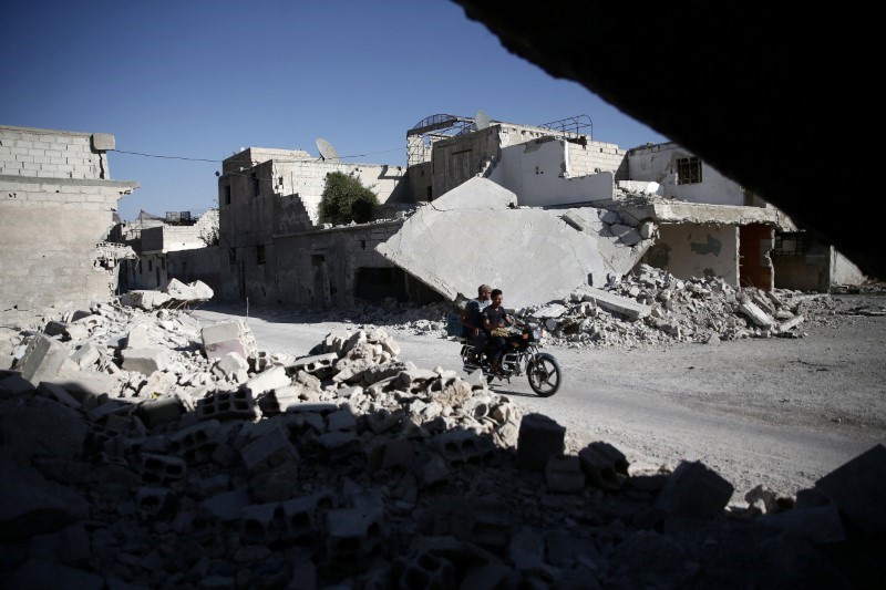 © Reuters. Men drive a motorcycle near damaged buildings in the rebel held Douma neighbourhood of Damascus