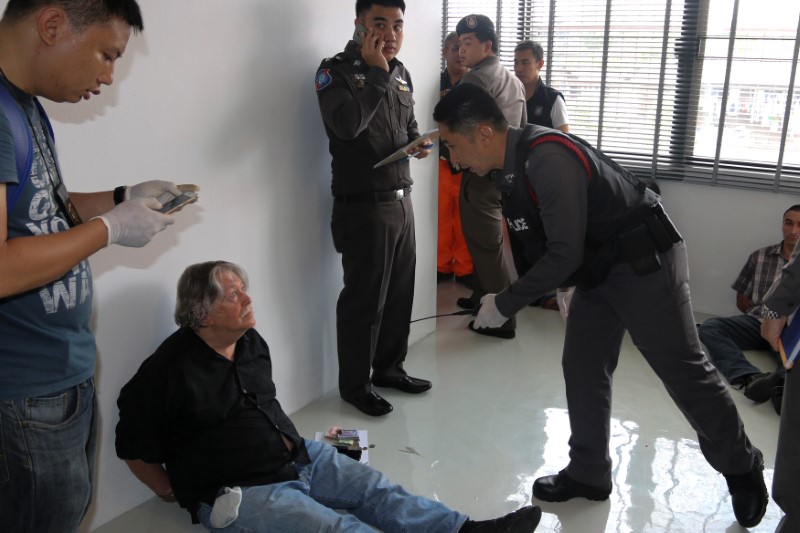 © Reuters. A foreign member of a suspected passport forgery gang is detained by police officers after a raid in Bangkok