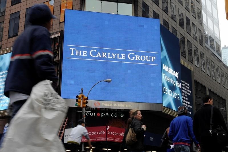 © Reuters. Passersby walk in front of video monitors announcing the Carlyle Group's listing on the NASDAQ market site in New York's Times Square after the opening bell for trading