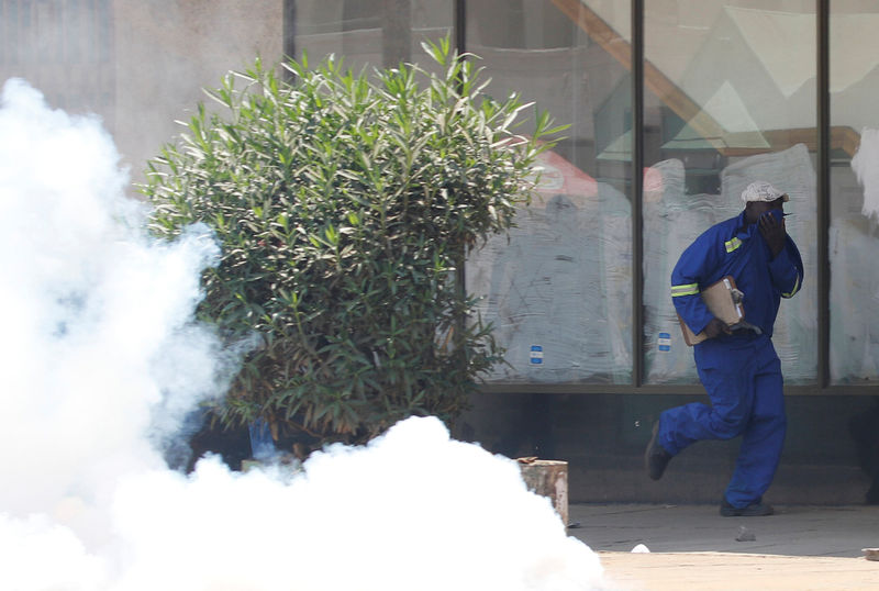 © Reuters. A man runs from teargas during clashes between police and street vendors in central Harare