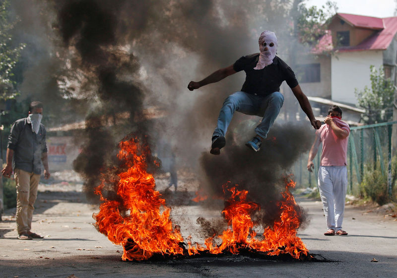 © Reuters. A man in a balaclava jumps over burning debris during a protest against the recent killings in Kashmir, in Srinagar